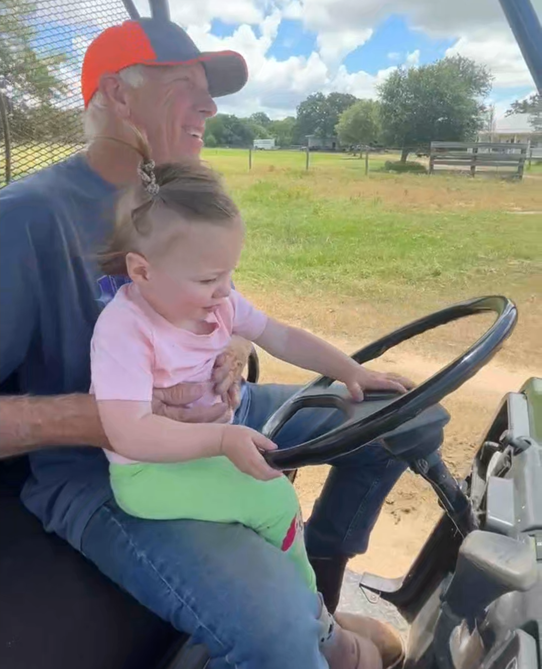 A grandfather driving a UTV with a toddler on his lap holding the steering wheel